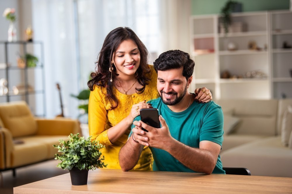 Indian,young,couple,using,smartphone,at,home